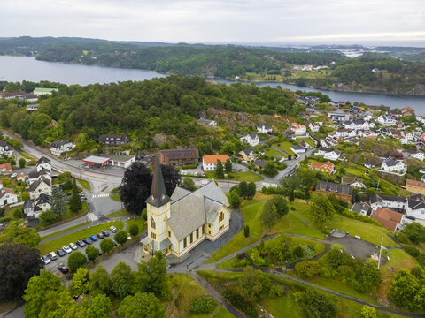 Aerial view of a quaint church standing proudly on a hill overlooking the town and the shimmering waters in the distance, Grimstad, Agder, Norway.