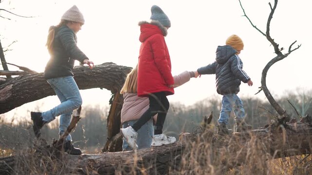 Children walking on fallen log across dry field at sunset wearing winter coat and knit hat while balancing together family sibling play outdoors nature exploration child boot adventure smile