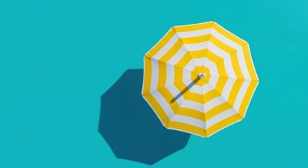 Top view of a yellow and white striped beach umbrella on a bright blue surface © ABDUL