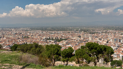 Expansive cityscape of Manisa, Turkey, showcasing the Manisa Twin Towers and residential areas under a dynamic cloudy sky