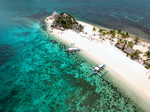 Aerial view of the vibrant turquoise waters meeting the white sandy shore of the island, boats resting near the coastline, Romblon, Philippines.
