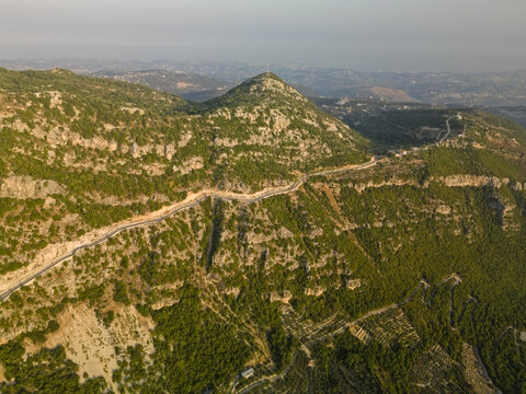 Aerial view of a winding road snakes along a rugged mountain ridge, contrasting with the lush green vegetation clinging to the steep slopes, Douma, North Governorate, Lebanon.
