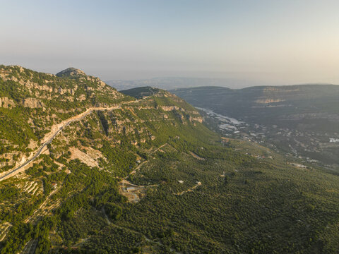 Aerial view of winding roads carving through the rugged, forested mountains, bathed in the warm glow of the sun, Douma, North Governorate, Lebanon.