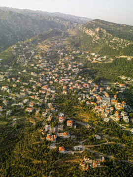 Aerial view of terracotta rooftops nestled amongst lush green hills, a serene blend of human habitat and nature's grandeur, Douma, North Governorate, Lebanon.