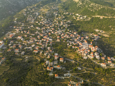 Aerial view of a serene town nestled amidst rolling hills, where terracotta rooftops punctuate the lush greenery, revealing a tranquil landscape, Douma, North Governorate, Lebanon.