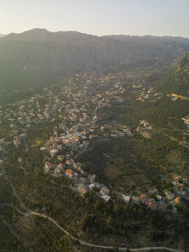 Aerial view of terracotta roofs punctuate the lush green landscape, nestled within rolling hills under a soft, golden light, Douma, North Governorate, Lebanon.