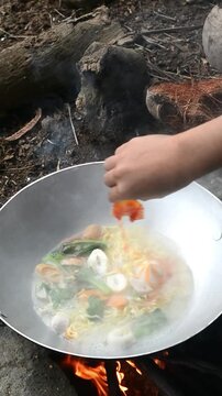 Cooking seblak with various toppings in a rice field using traditional outdoor style. Popular Indonesian spicy street food prepared in a rustic countryside atmosphere, featuring authentic culinary cul