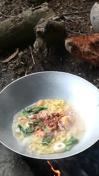 Cooking seblak with various toppings in a rice field using traditional outdoor style. Popular Indonesian spicy street food prepared in a rustic countryside atmosphere, featuring authentic culinary cul