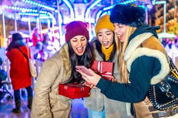 Excited friends sharing christmas gifts and using smartphone at christmas market