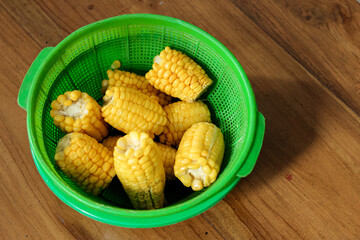 Close-up high angle photo of some boiled yellow sweet corn in a green bowl placed on a lacquer table