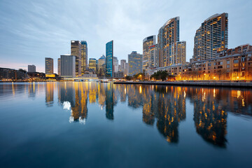 Fototapeta premium Close up, City skyline reflected in calm river at dusk