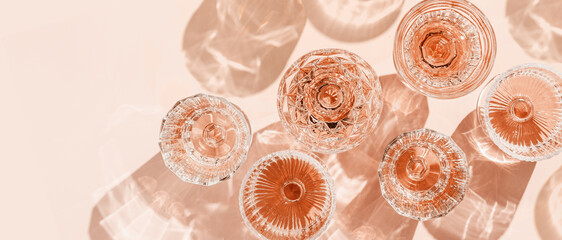 Minimal summer party concept, set glasses of rose wine or champagne on pink with shadows and light reflections. Bright shine wineglass with sparkling alcohol drink at sunlight, top view monochrome