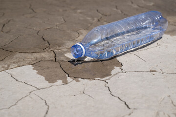 Drinking water drips from a plastic bottle onto heat-cracked clay in the desert