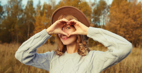 Beauty portrait of stylish happy young woman showing heart gesture, girl smiling in autumn park