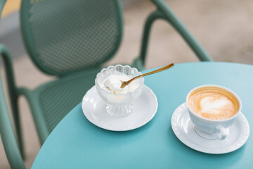 Vanilla ice cream in a glass bowl, a cup of cappuccino on a blue garden table on summer terrace.