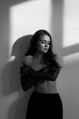 A woman poses confidently in a black and white setting, with her arms crossed and shadow play enhancing her expression. Bright light streams through a window at midday