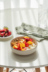 Granola or muesli with natural greek yogurt, strawberry and peach in a bowl on a white table near window