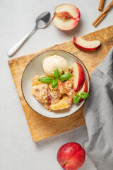 Peach crumble or cobbler with vanilla ice cream scoops and cinnamon in a plate on a wooden board