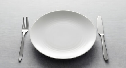 Empty white dinner plate set on a clean table with a polished silver fork and knife, ready for a meal or reflecting a moment of culinary anticipation