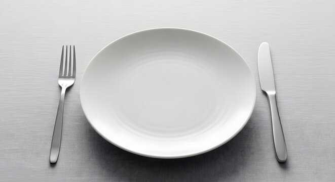 Empty white dinner plate set on a clean table with a polished silver fork and knife, ready for a meal or reflecting a moment of culinary anticipation