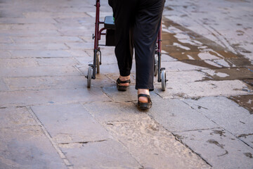 
An elderly person walks with the aid of a mobility aid along a sunny urban path