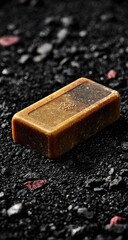 Rectangular bar of brown soap rests on dark gravel