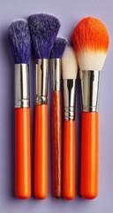 Five makeup brushes with orange handles and various brush heads stand on purple background