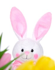 Obraz premium A cheerful, plush Easter bunny toy, with vibrant pink ears and a white body, is partially hidden behind yellow tulips.