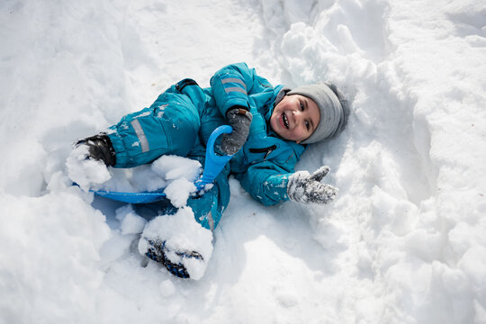 Happy child lying in snow enjoying winter fun with sled