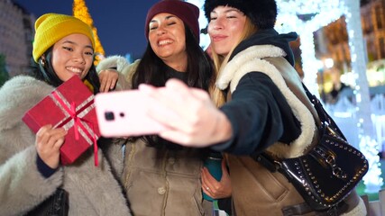 Cheerful friends taking christmas selfies in festive city at night - Powered by Adobe