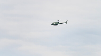 A helicopter is flying in the sky. The sky is cloudy and the helicopter is flying low