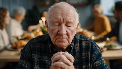 An elderly man with closed eyes prays at a festive dinner table before a meal, embodying the tradition of gratitude during a thanksgiving family gathering and the concept of faith