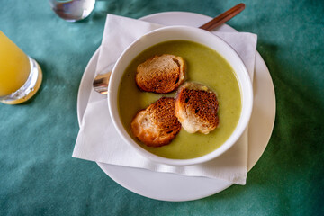 Pea soup with fried bread piece in bowl, napkin, plate and juice on table.
