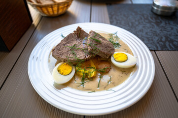 Stewed beef with boiled egg and potato in spicy aromatic dill sauce on white plate.
