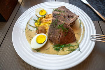 Boiled beef and egg in dill sauce, white plate.