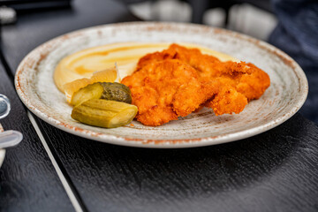 Breaded fried schnitzel with mashed potato and pickled cucumber.