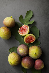 Fresh figs placed on top of green leaves on black table.