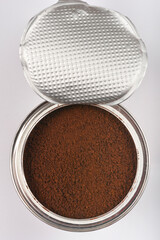 A cylindrical metal can with a partially peeled-off silver foil lid reveals dark brown instant coffee granules inside