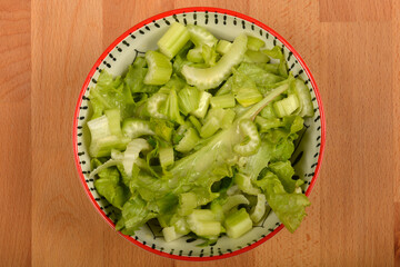 A high-angle shot of a green salad with lettuce and chopped celery in a decorated bowl on a wooden board