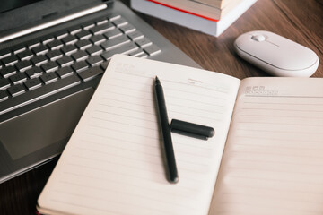 A pen and open notebook on a wooden desk, with a wireless mouse and laptop in the background. This clean image represents planning, work, and productivity.