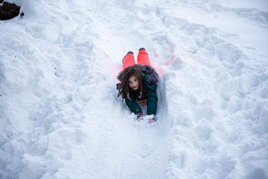 Girl lying on sled sliding down snowy hill in winter - Powered by Adobe