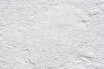 A close-up of a weathered, painted white wall with a rough and textured surface, showing traces of age and imperfections