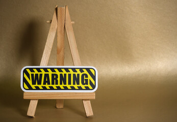 Yellow and black warning sign on wooden easel against golden background, symbol of caution and attention.