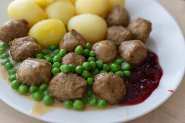 A plate of ikea-style meatballs with boiled potatoes, green peas, and lingonberry jam, concept of home cooking, swedish cuisine, and casual dining.