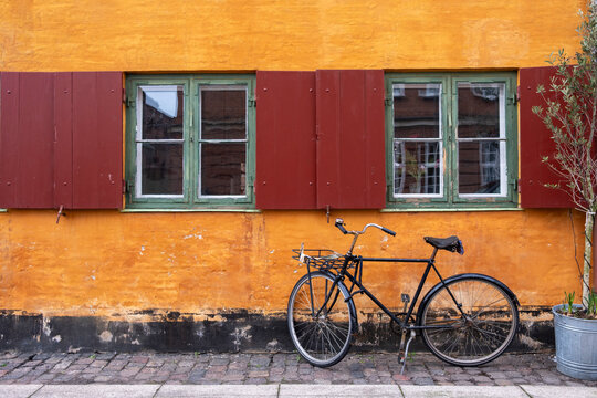 Bicycle against ochre wall with red shutters in Nyboder Copenhagen Denmark, historic quarter reflecting cultural heritage, cycling tradition and urban sustainability