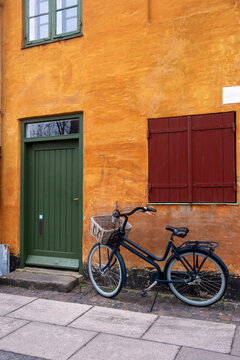 Bicycle parked by ochre house in Nyboder Copenhagen Denmark with green door and red shutters, capturing historic architecture, urban charm, cycling lifestyle and culture