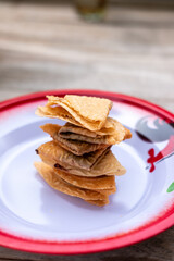 A stack of crispy, folded Indonesian Kue Semprong cookies rests on a traditional enamel plate with a vintage red border.