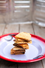 A stack of crispy, folded Indonesian Kue Semprong cookies rests on a traditional enamel plate with a vintage red border.