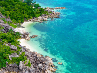 Aerial view of Praslin Island, Seychelles, featuring lush green hills, tropical coastline, and calm turquoise waters under a partly cloudy sky.
