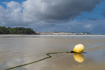 Bouée jaune sur le sable humide à marée basse, reflet dans l’eau, avec la ville de Douarnenez...